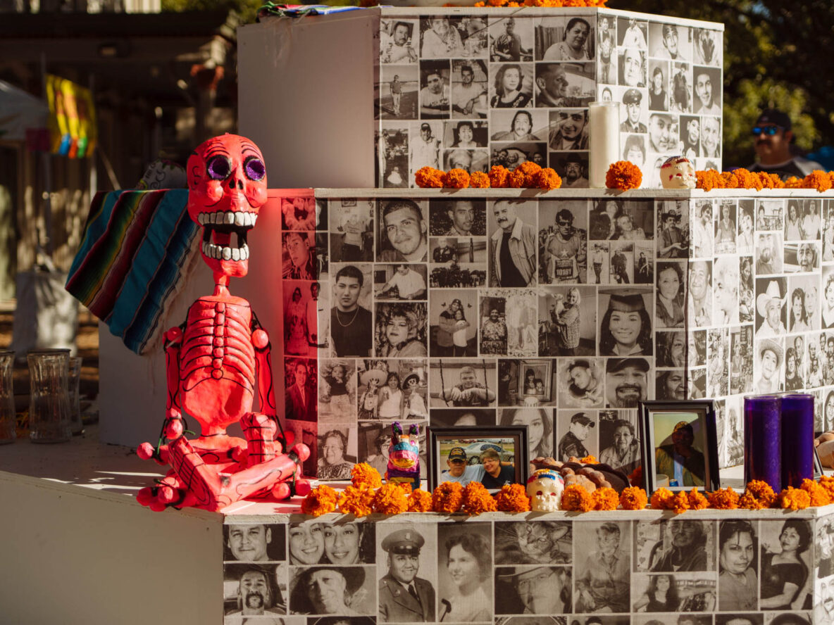 A pink skeleton figure sits among pumpkins and black-and-white photos.