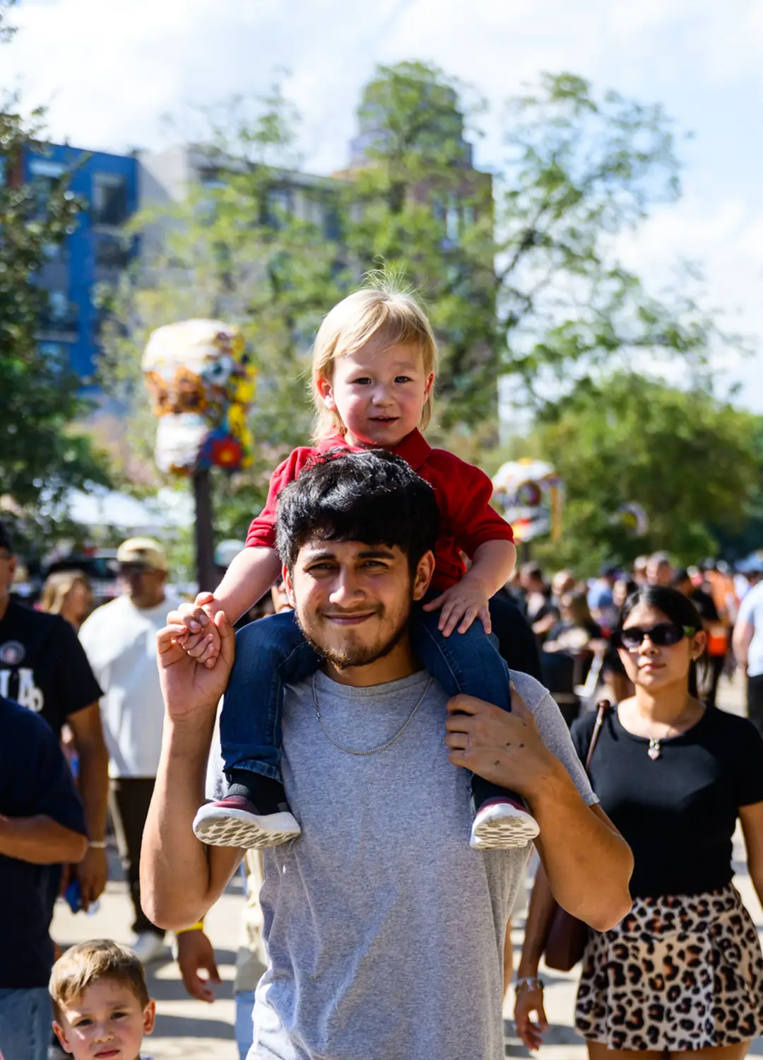 Smiling little boy riding on his father’s shoulders among the crowd at Muertos Fest
