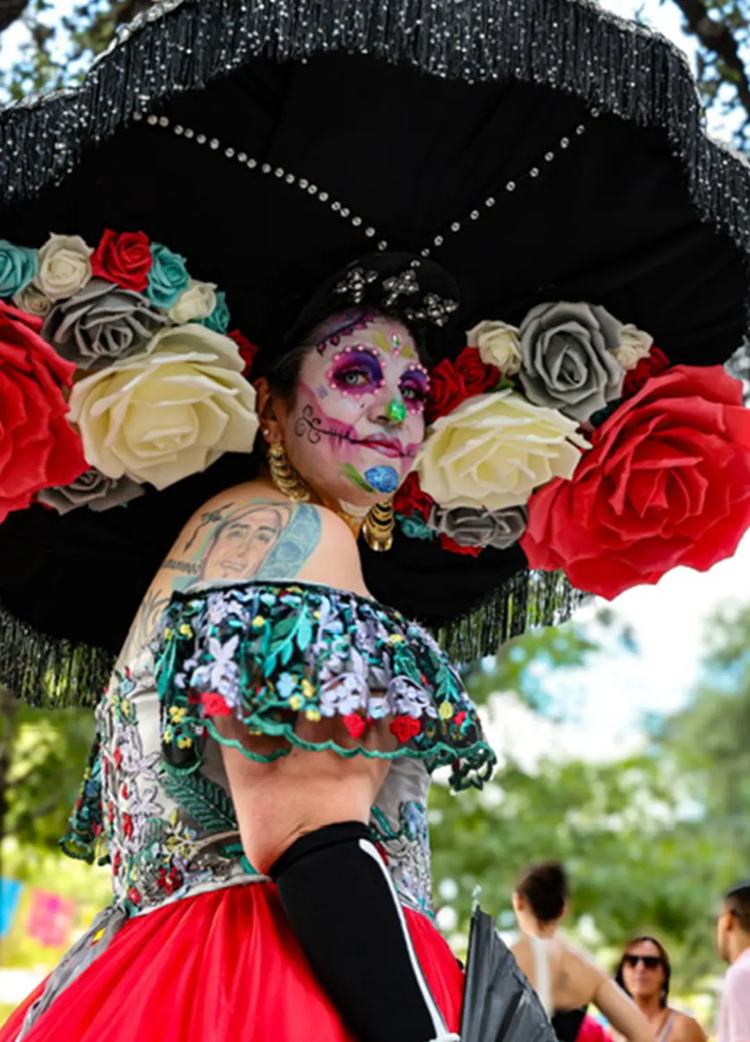 Catrina wearing calavera makeup and an elaborate floral headpiece with oversized red and white flowers