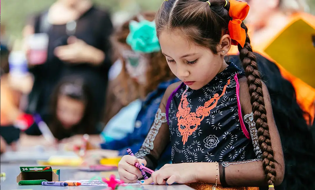 Child getting creative during a hands-on art workshop at Muertos Fest
