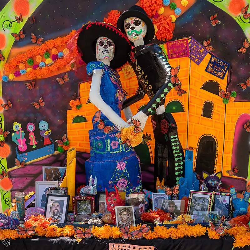 Colorful Día de los Muertos altar featuring a couple dancing surrounded by flowers and papel picado