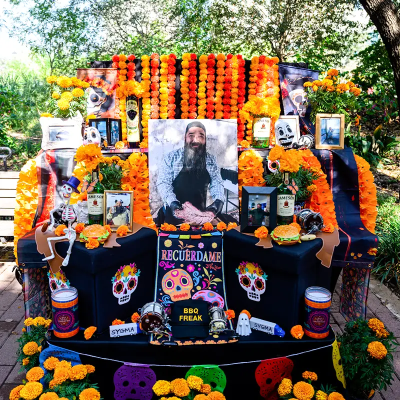 Día de los Muertos altar honoring a loved one with photographs, marigolds, food, and personal mementos at Muertos Fest