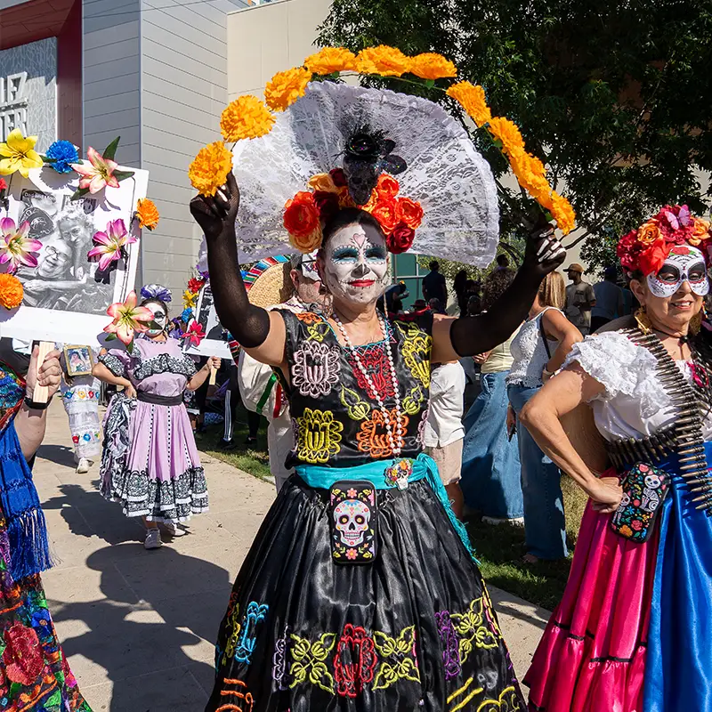 Catrina procession participant in a black and orange floral headdress carrying a halo of marigolds at Muertos Fest