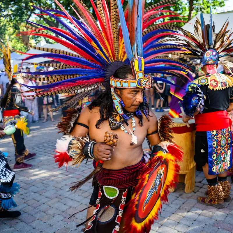 Indigenous dancer wearing a large multicolored feather headdress during the Muertos Fest procession