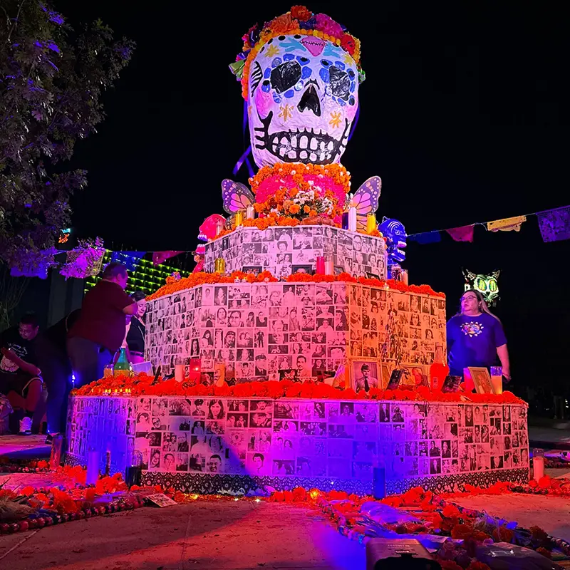 Living community altar illuminated at night with photographs of loved ones at Hemisfair during Muertos Fest