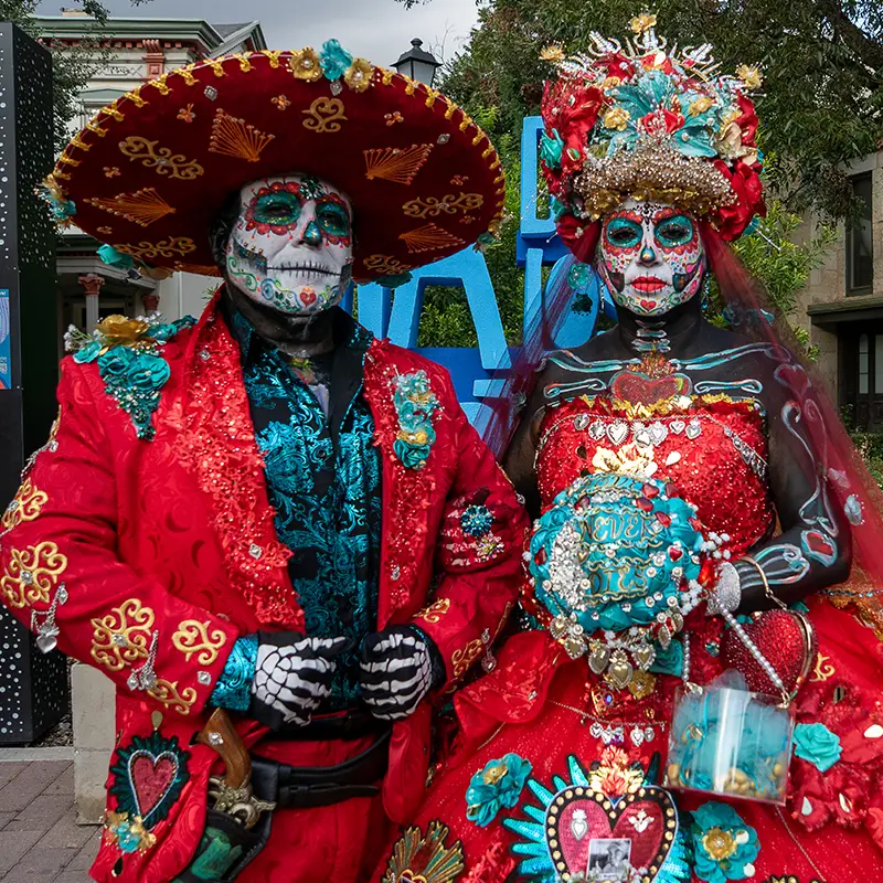 Elaborately dressed red Catrín and Catrina with calavera makeup at Muertos Fest