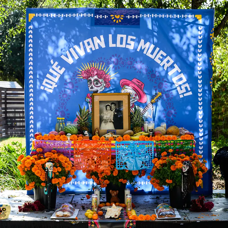 Community workshop creating Día de los Muertos ofrendas with photographs, flowers, and traditional offerings at Muertos Fest in San Antonio