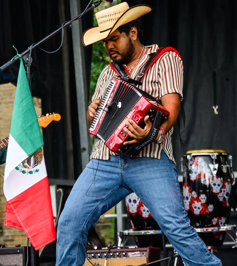 Tejano accordionist performing beside the Mexican flag on stage at Muertos Fest