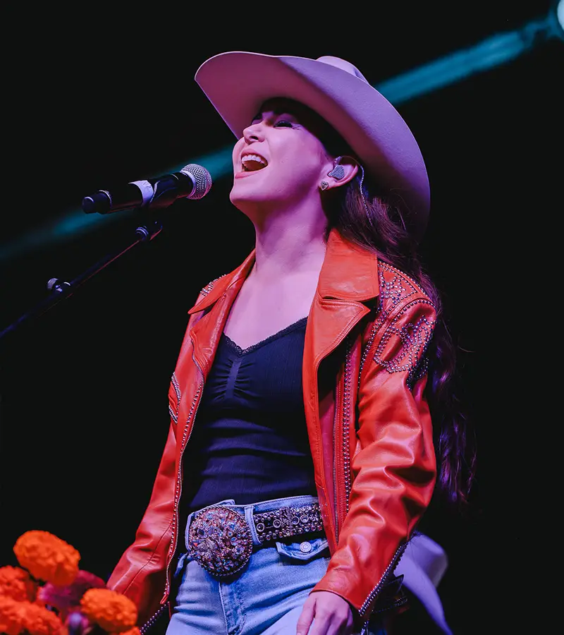 Female vocalist in cowboy hat performing on stage during Muertos Fest in San Antonio